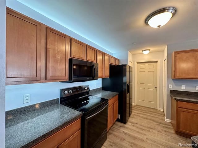 Kitchen with wood cabinetry, stone-look counters and black appliances